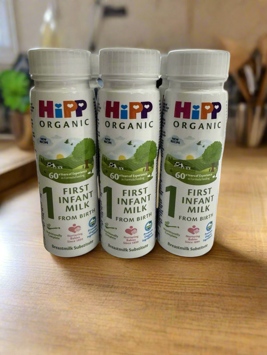 Six bottles of HiPP Organic First Infant Ready to Drink Milk on a modern wooden kitchen counter surface.