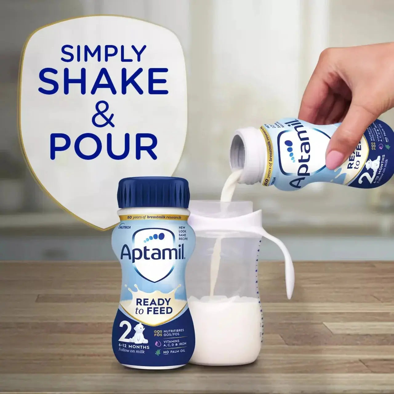 Aptamil Ready to Feed bottle and container with text 'Simply Shake & Pour' on a wooden surface.