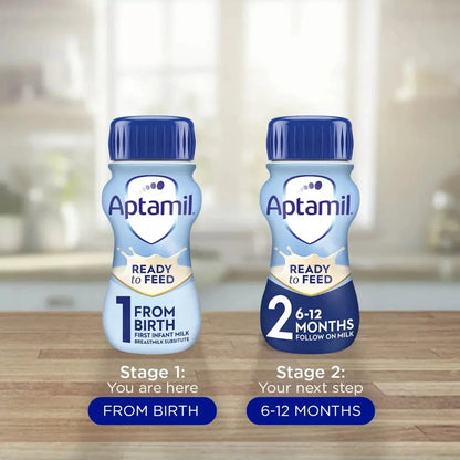 Two Aptamil Ready to Feed bottles on a wooden surface with a blurred kitchen background.
