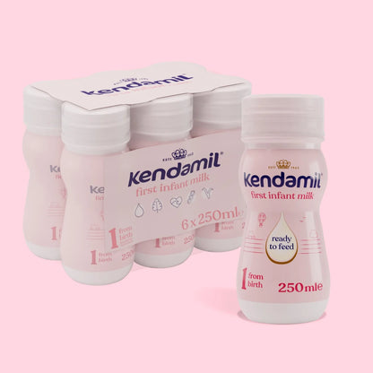 Kendamil first infant milk bottles and packaging on a pink background