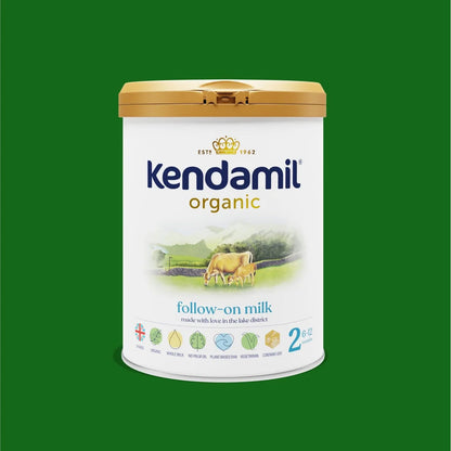 A canister of Kendamil Organic Follow-on Milk, size 2, featuring a white label with a gold lid, set against a solid green background.