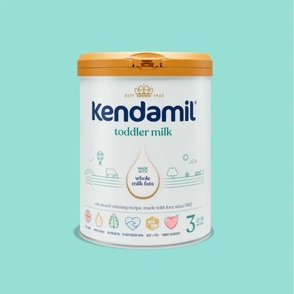 A canister of Kendamil toddler milk powder on a solid light teal background. The canister is white with a mustard yellow lid and features the brand name 'Kendamil' in blue, along with 'toddler milk' and 'whole milk fats' text.