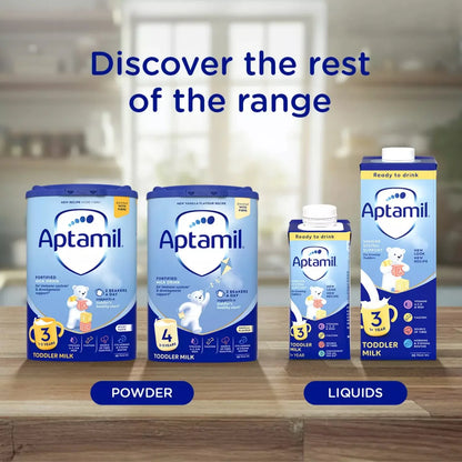 Aptamil milk products including powder and liquids on a wooden surface with a blurred kitchen background.