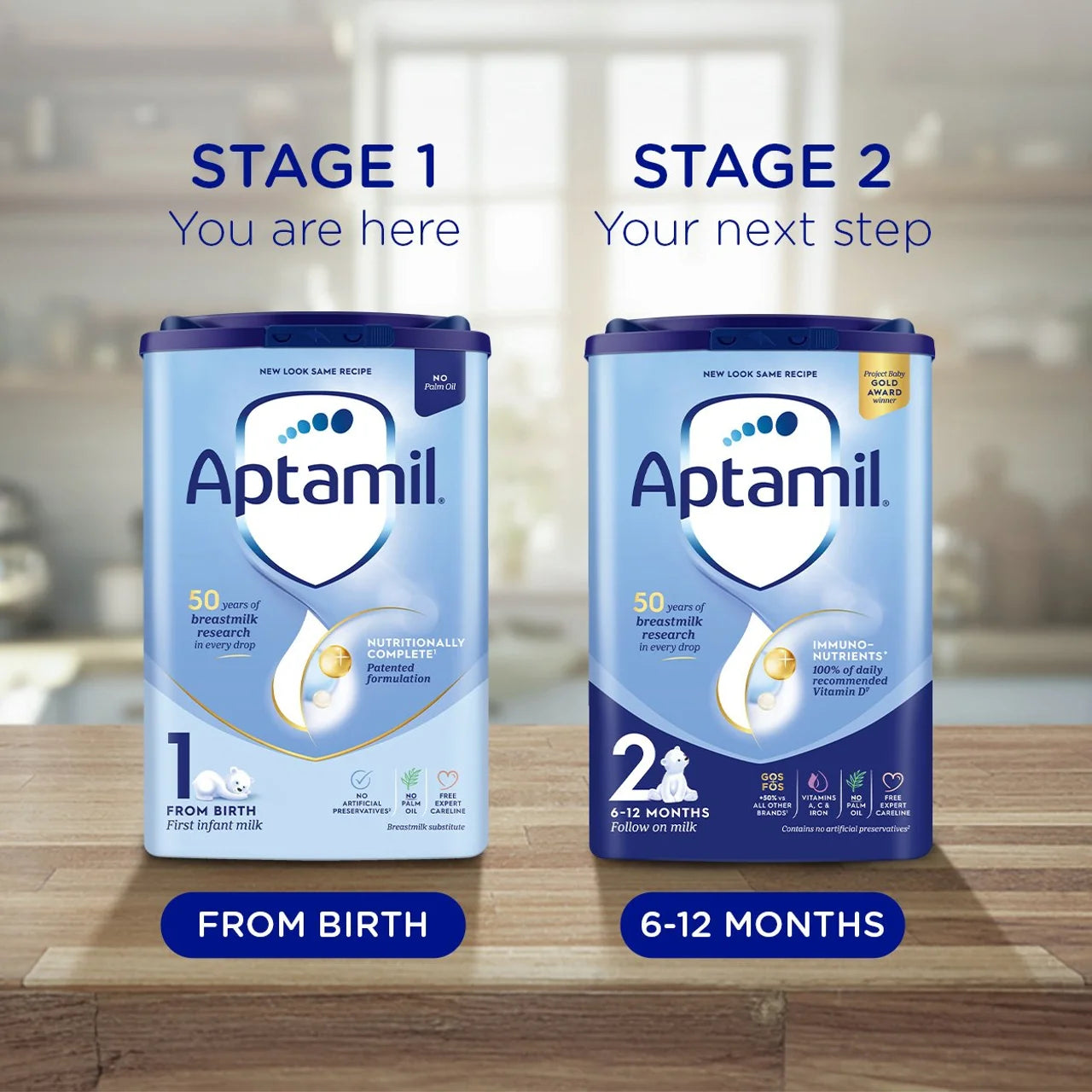 Two Aptamil baby formula cans labeled 'Stage 1' and 'Stage 2' on a wooden surface.