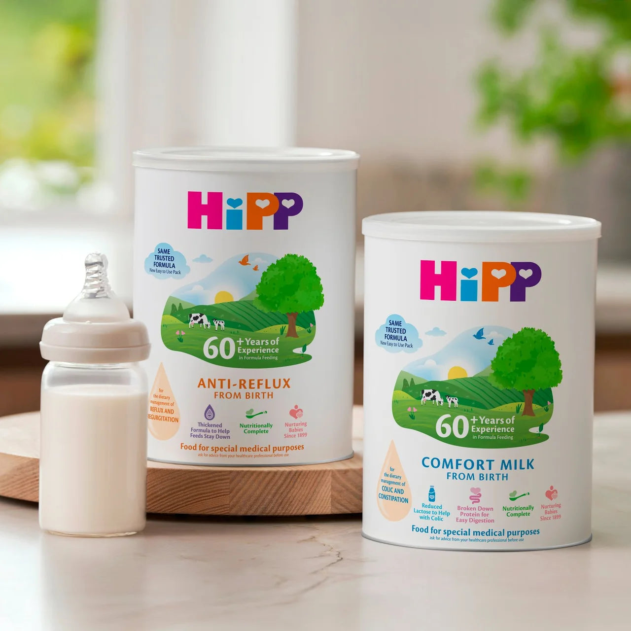 Two HiPP baby formula cans with a bottle on a wooden surface.