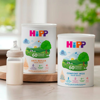 Two HiPP baby formula cans with a bottle on a wooden surface.