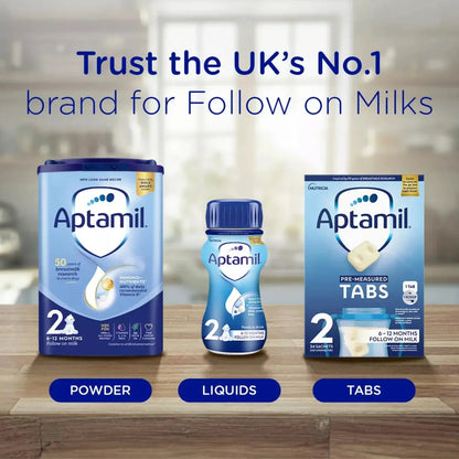 Aptamil milk products including powder, liquids, and tabs on a wooden surface with a blurred background.