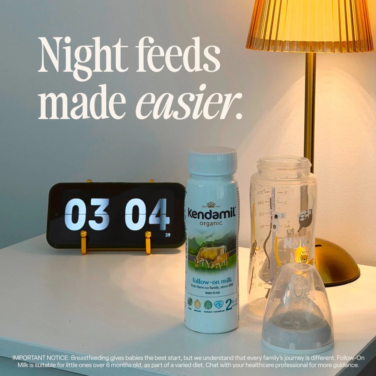 Kendamil organic milk bottle with a digital clock and lamp on a nightstand.