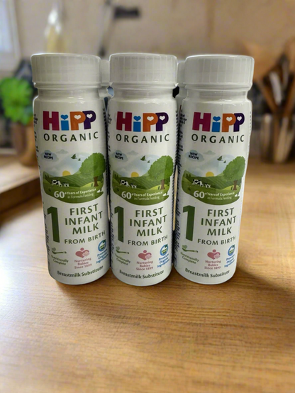 Six bottles of HiPP Organic First Infant Ready to Drink Milk on a modern wooden kitchen counter surface.