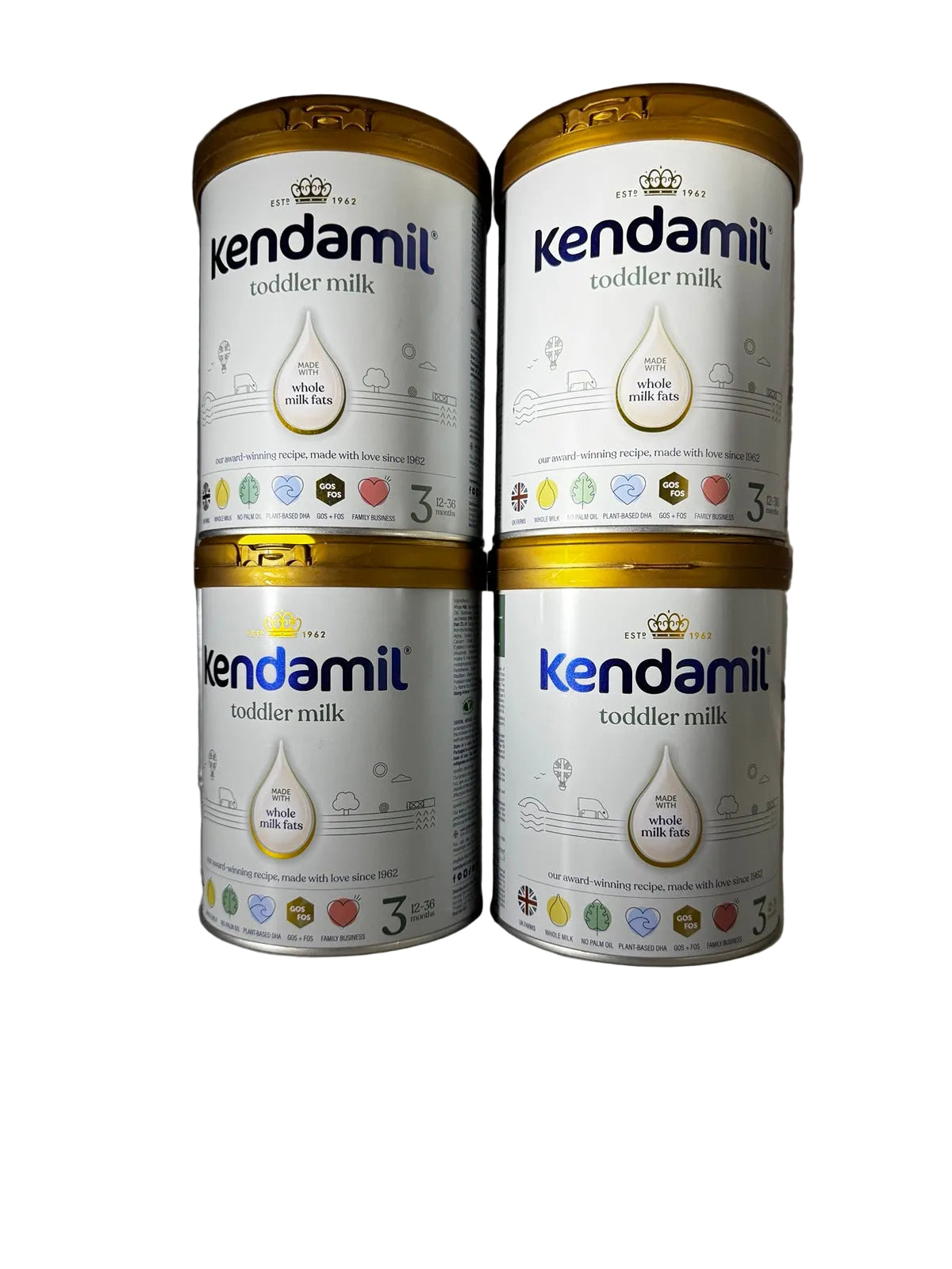 Four cans of Kendamil toddler milk powder arranged in a 2x2 stack on a light gray surface against a dark gray corrugated background.
